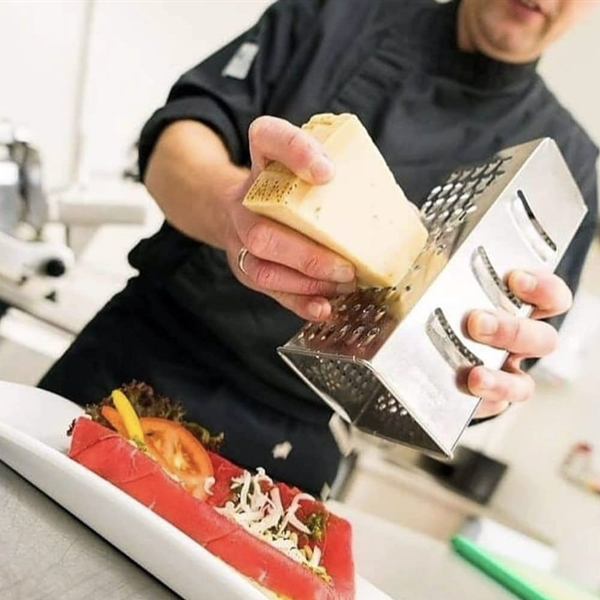 Onze chef raspt kaas over een broodje carpaccio